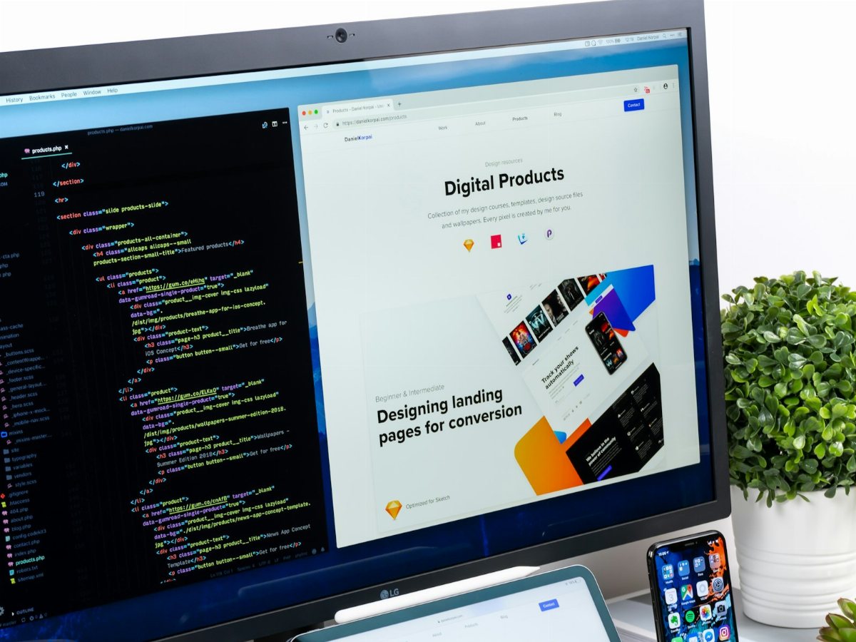 A web developer's workstation: code beside the finished website design, with the mobile app on a phone